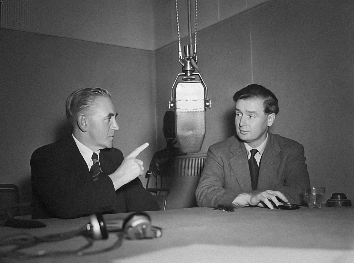 Two men talk into a microphone during a radio broadcast.